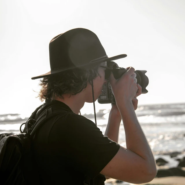 a man in a hat taking pictures of the ocean