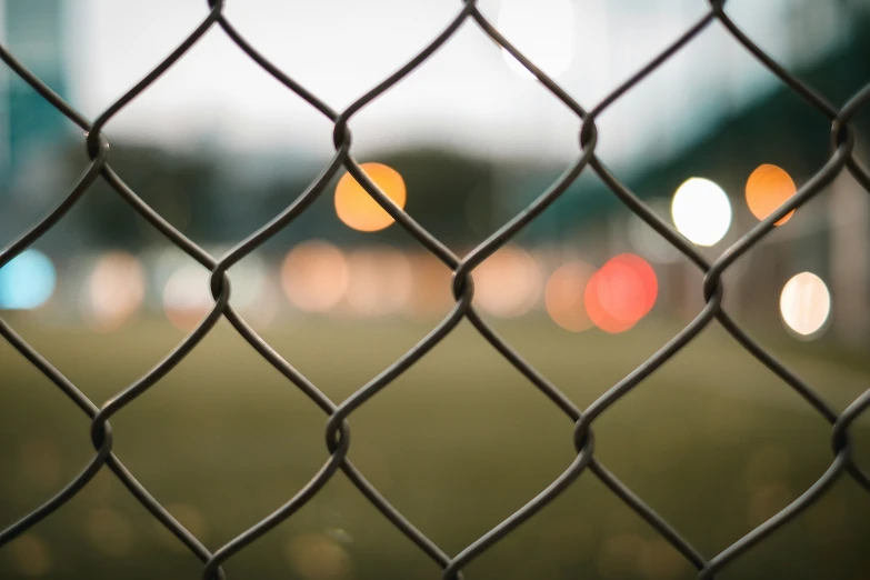 a fence with a field and lights behind it