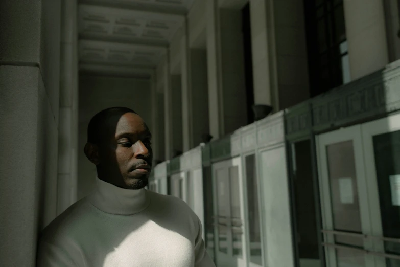 a black man with a sweater on and his head down stands in front of a building