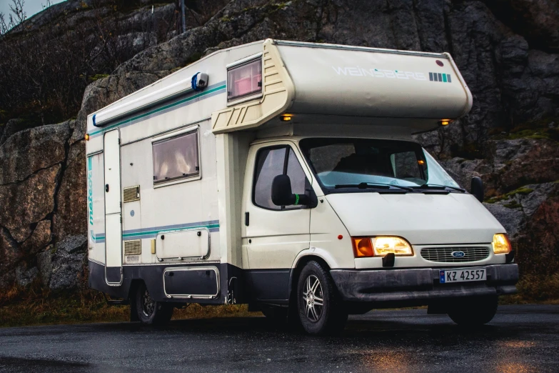 a white van sitting beside a mountain on a wet road