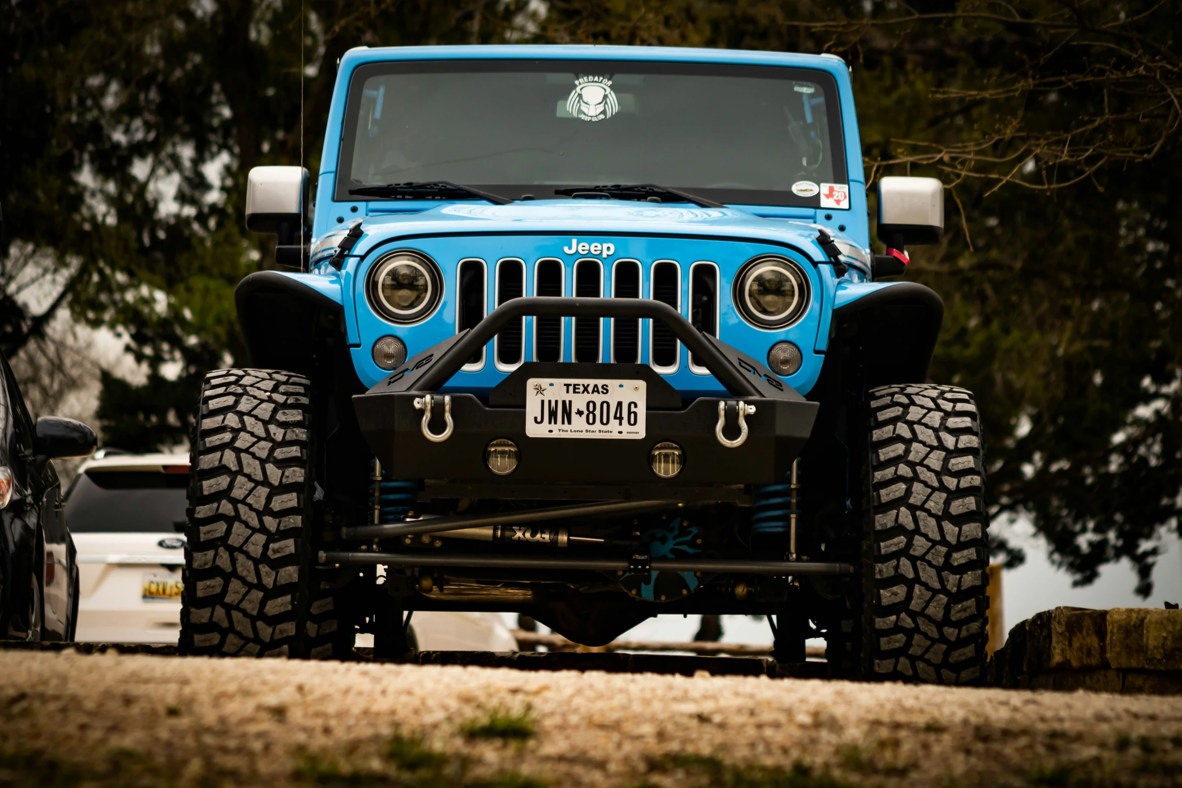 a blue jeep sits parked beside other cars