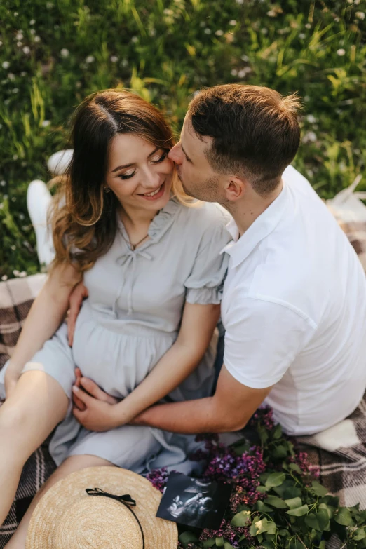 a pregnant couple smiling and cuddling while they are sitting on the ground