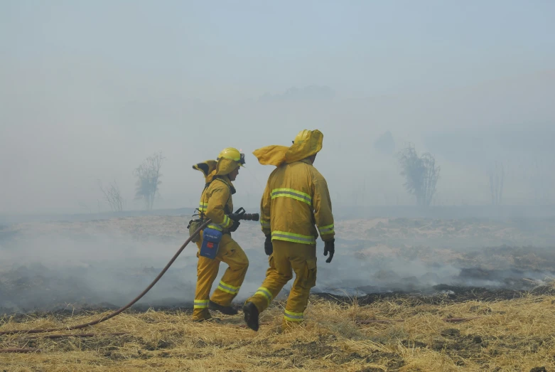 two firefighters walk down a grassy field while fighting a fire