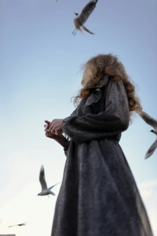 a girl standing on top of a sidewalk near birds