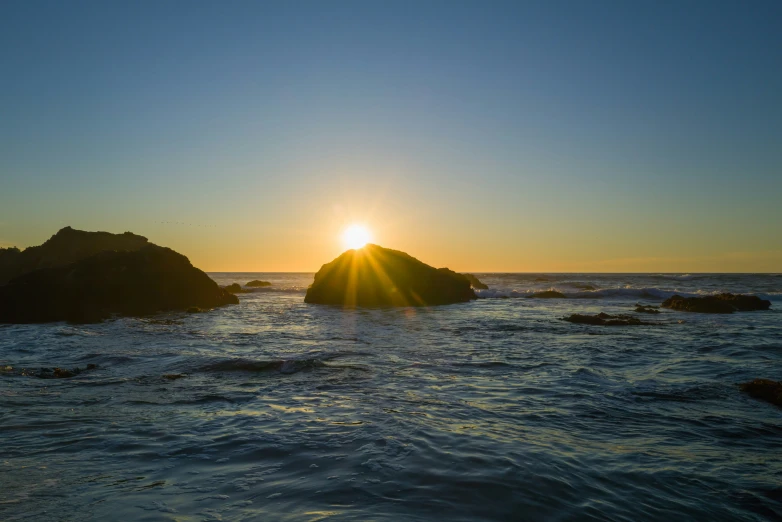 sun setting behind the ocean with a rock in front