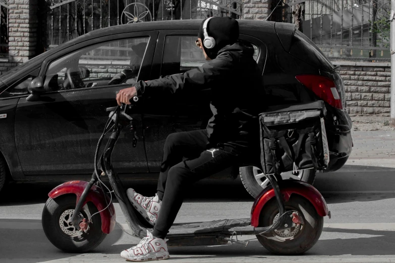 a man wearing headphones riding a scooter next to a parked car