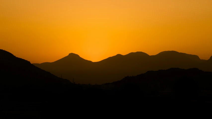 a sunset seen over mountains with a bird flying in the air