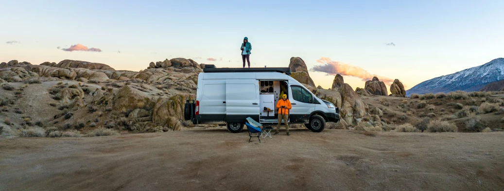 an van with a person standing on top of it parked in front of some mountain