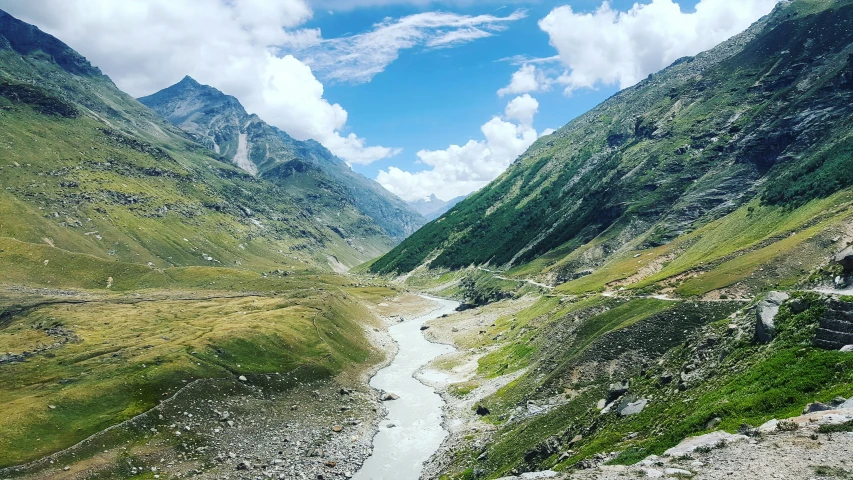 a narrow mountain river is in the middle of a grassy valley