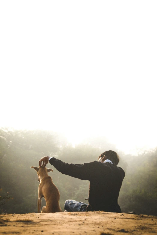 a person that is kneeling in the dirt with a dog