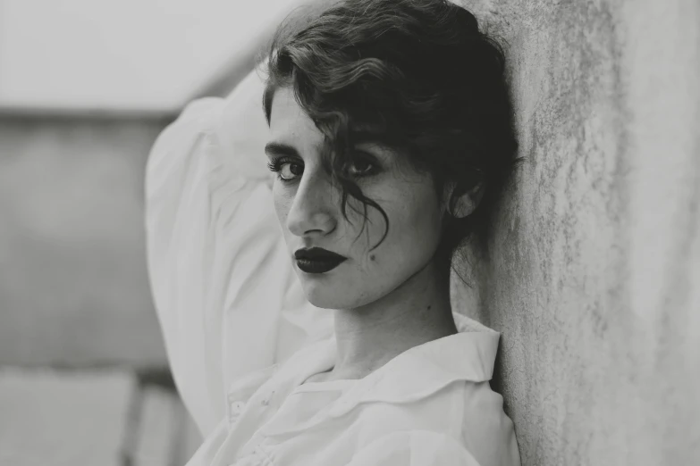 a girl with black lipstick and makeup looking down while leaning against a wall