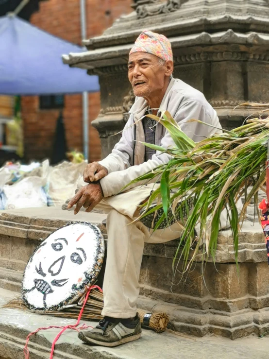 an elderly man sitting on a pillar with a wreath next to him