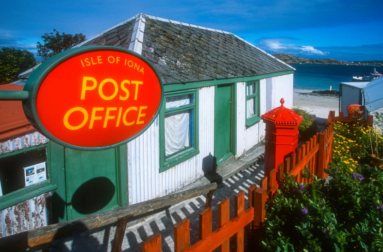 a red post office sign in front of a white building