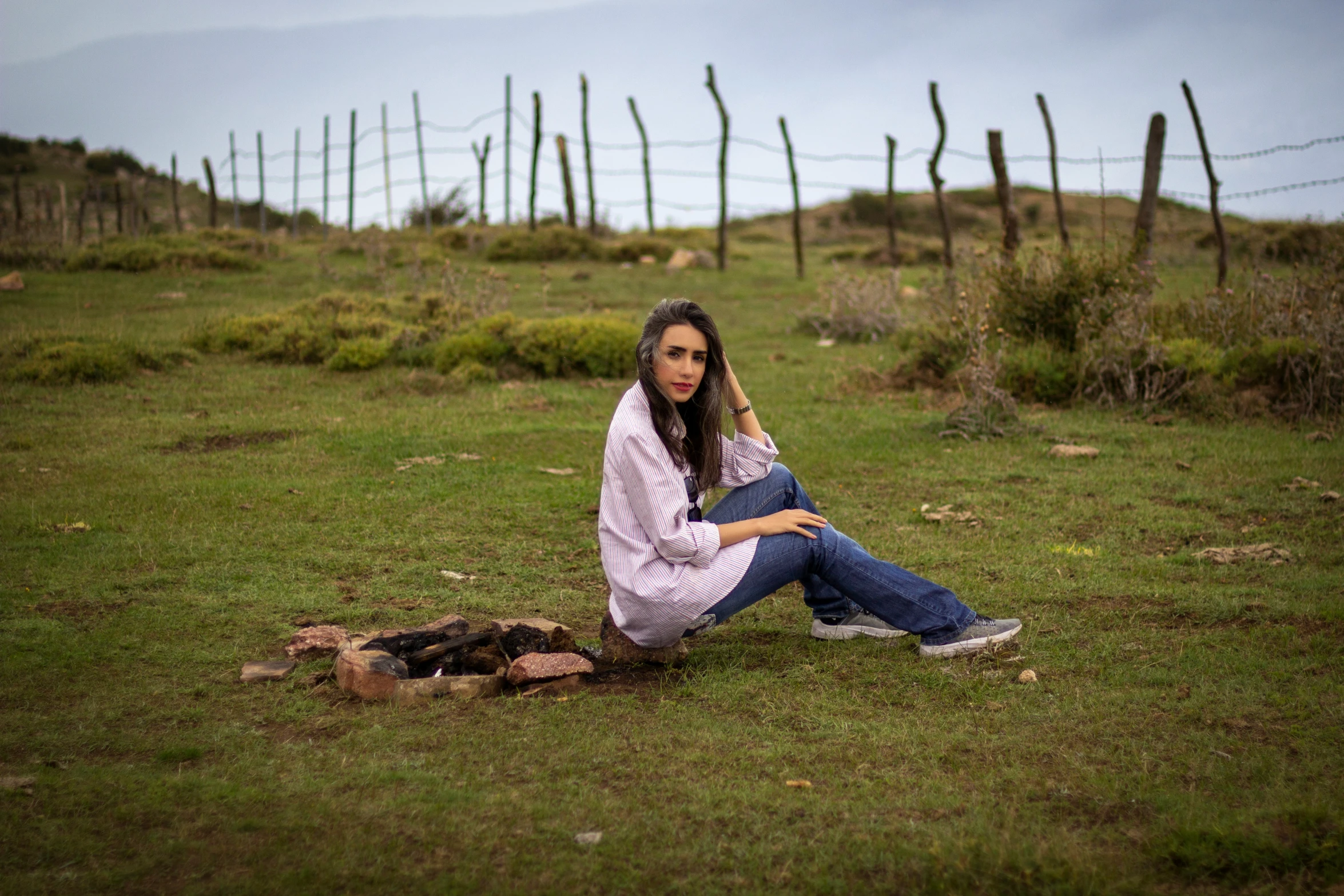 a woman in a pink sweater and jeans sitting in a field