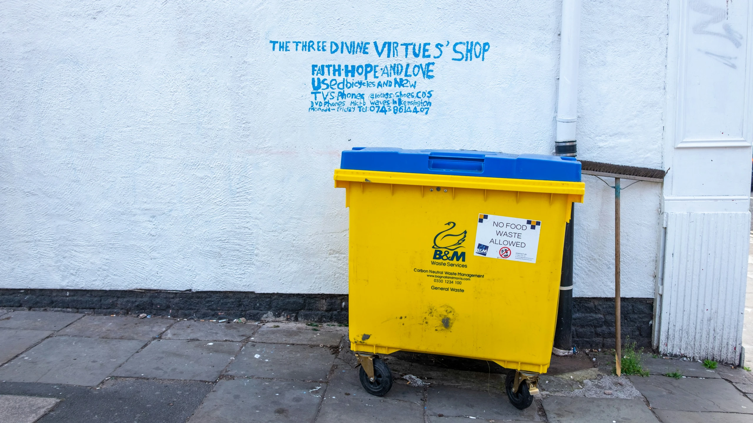 a yellow trashcan outside of a building with graffiti on the side