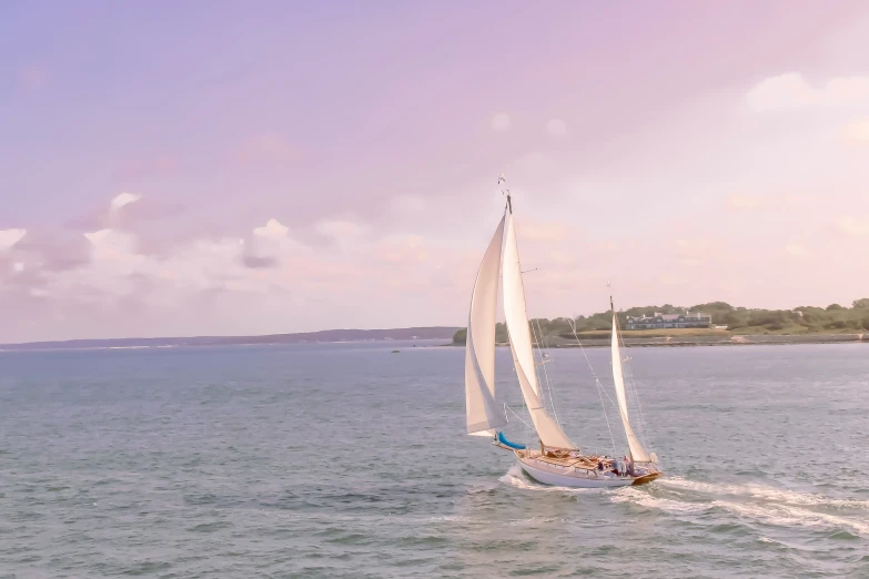 a sailboat travels on a calm ocean with an island in the background