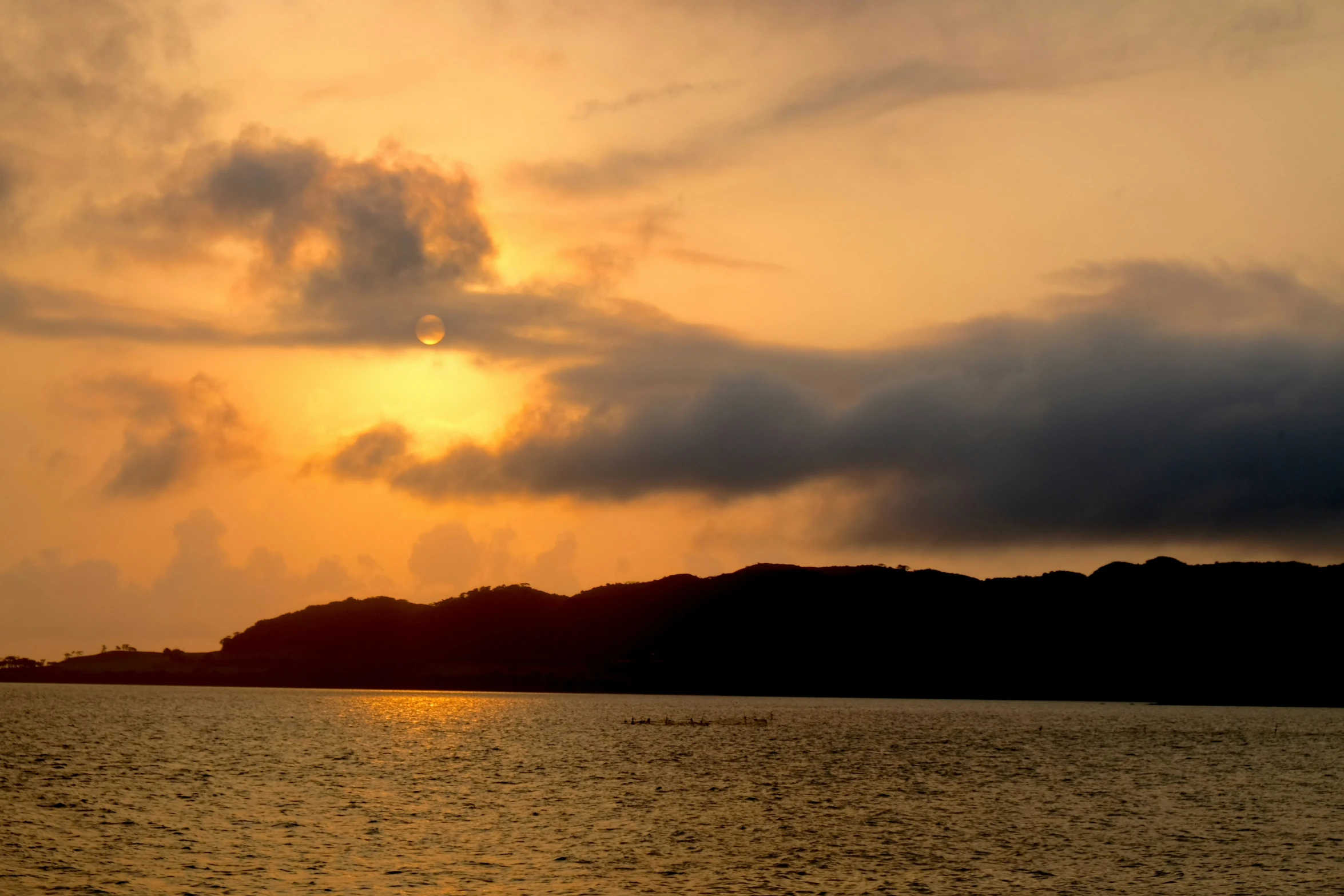 the sun rising over a hill and water