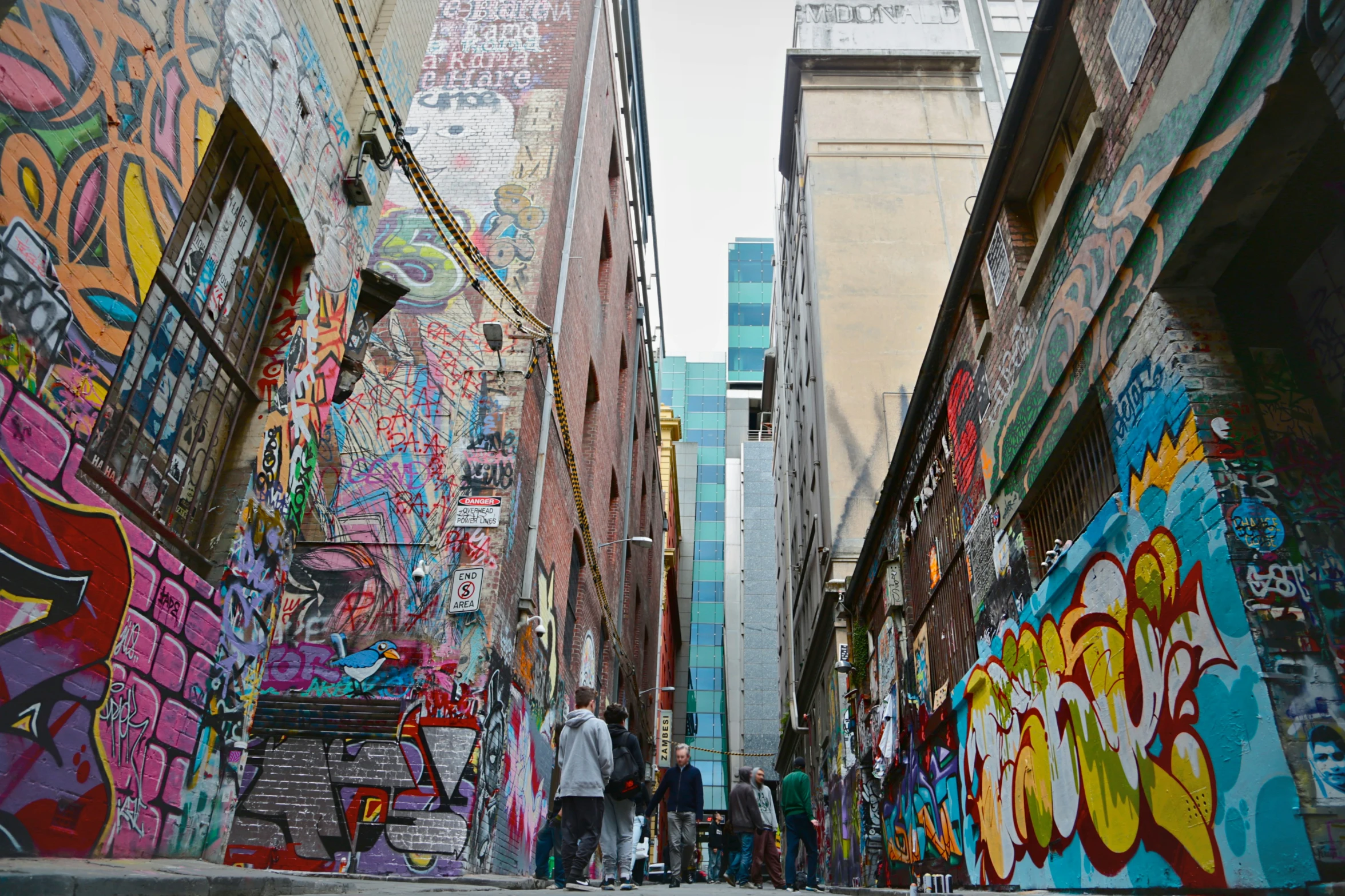 many people walking down an alley with a mural on the side