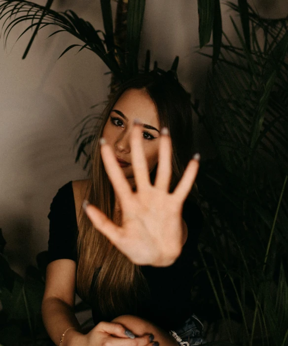 a woman is sitting in front of plants and pointing her hand up