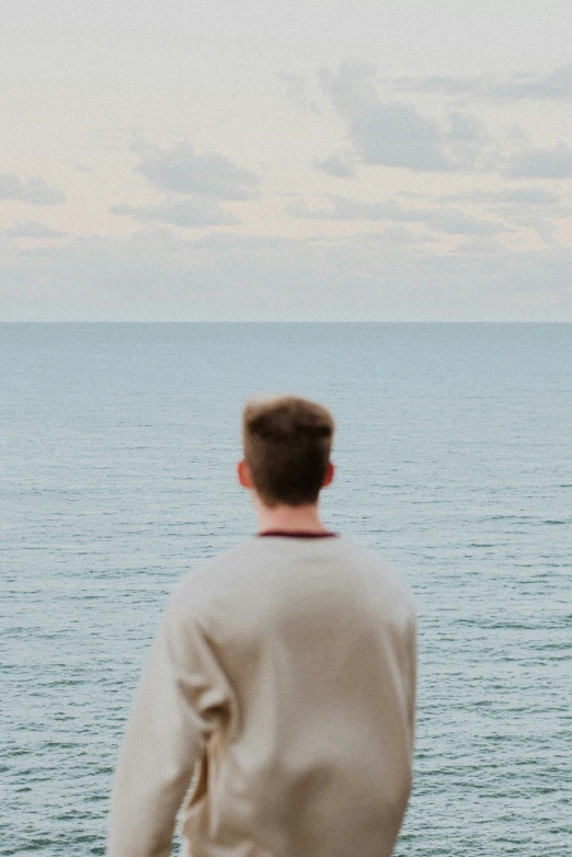 a man stands looking at the water on a cloudy day