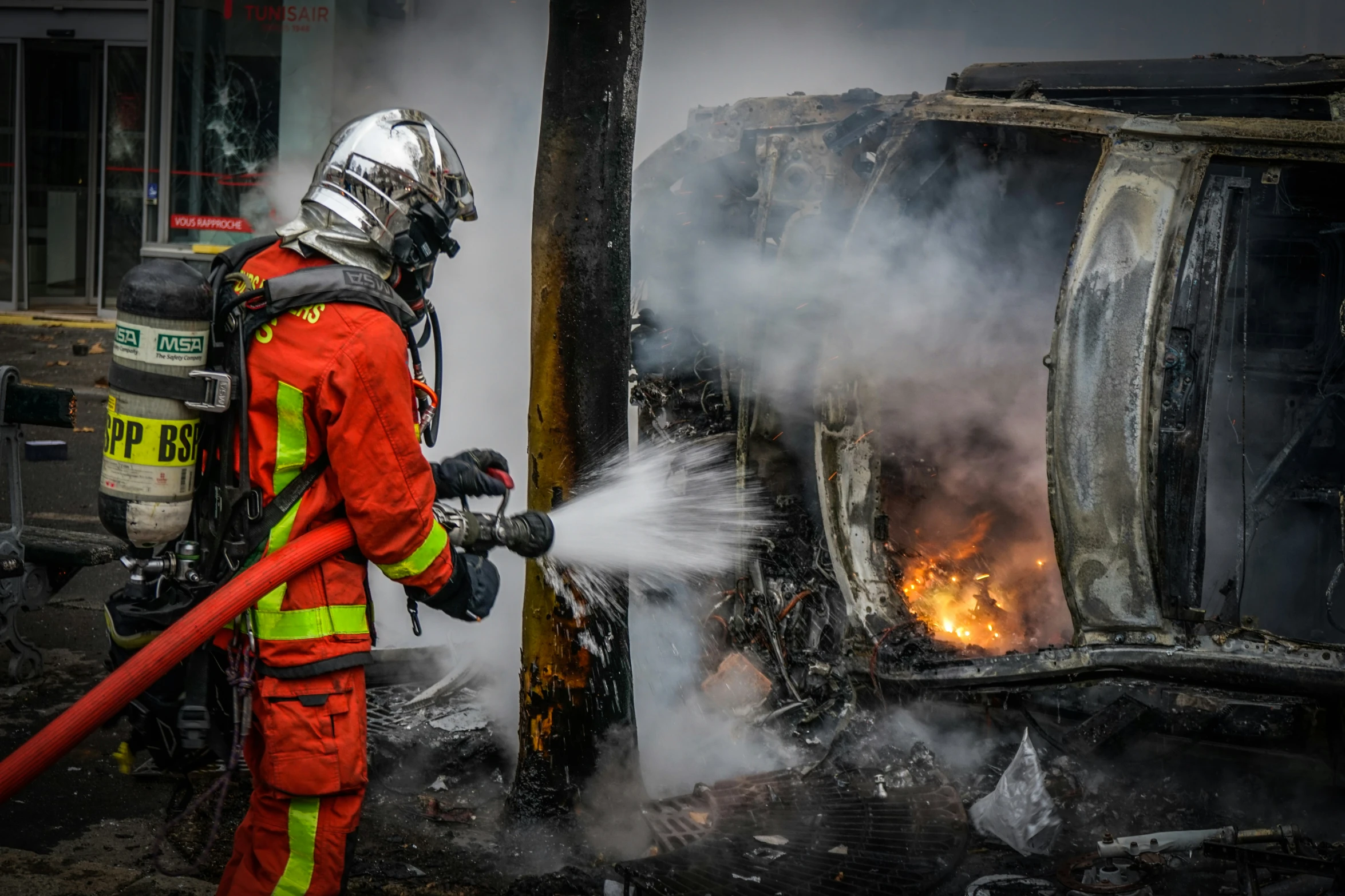 a fire fighter spraying out a fire near a burned building