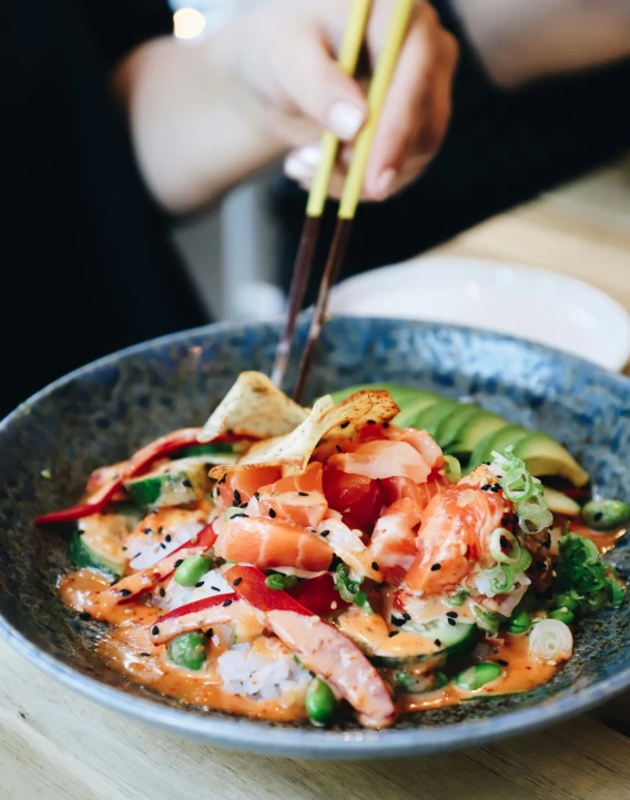 a person holds chop sticks over a bowl of salmon