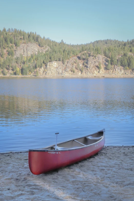 a red boat sits in the water near a lake