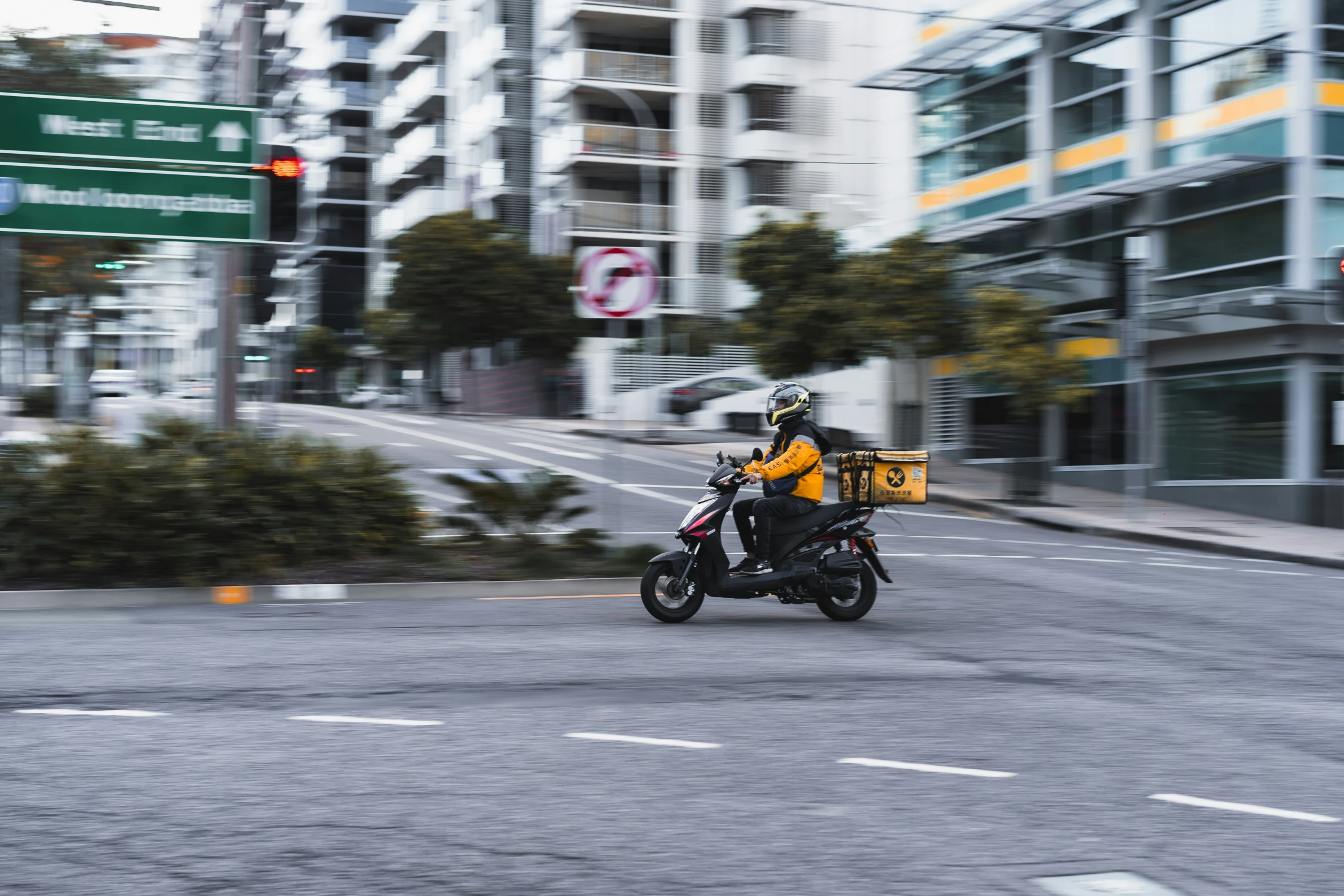 person in an orange jacket riding a black motorcycle down the road