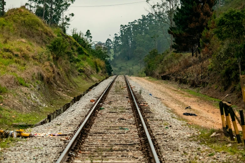 the railway is empty, with rocks and green trees on each side