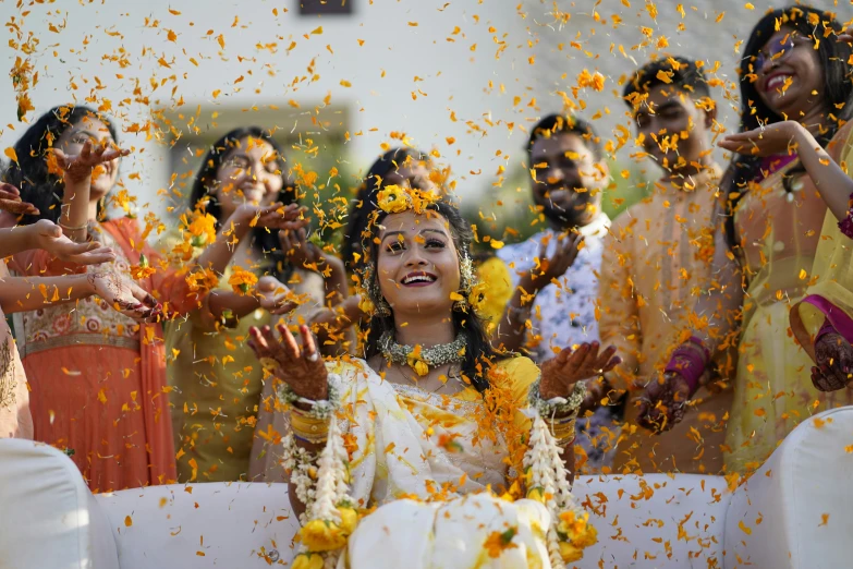 a bride in a yellow dress and orange garland throwing yellow flowers