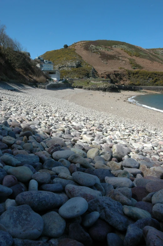 a beach with large rocks by the water and hills in the background