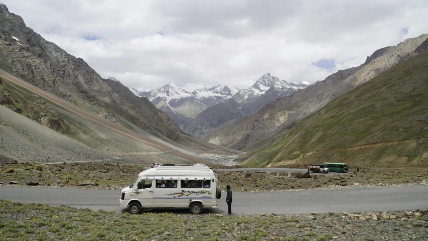 a white bus and its driver on the side of a mountain road