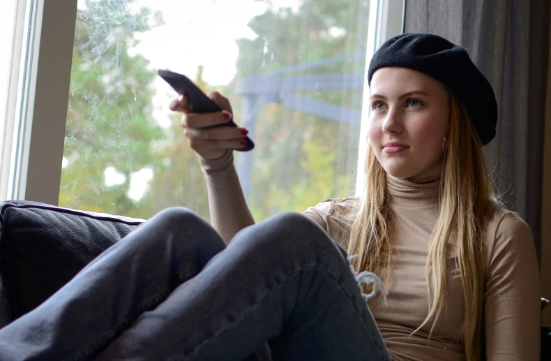 a girl with long hair sitting on the couch and holding a cell phone