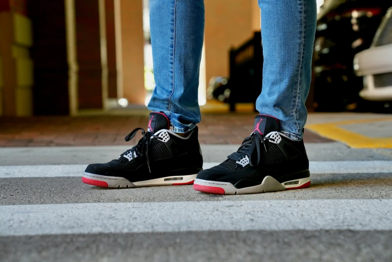 person in black and pink sneakers with blue jeans standing at the end of a street