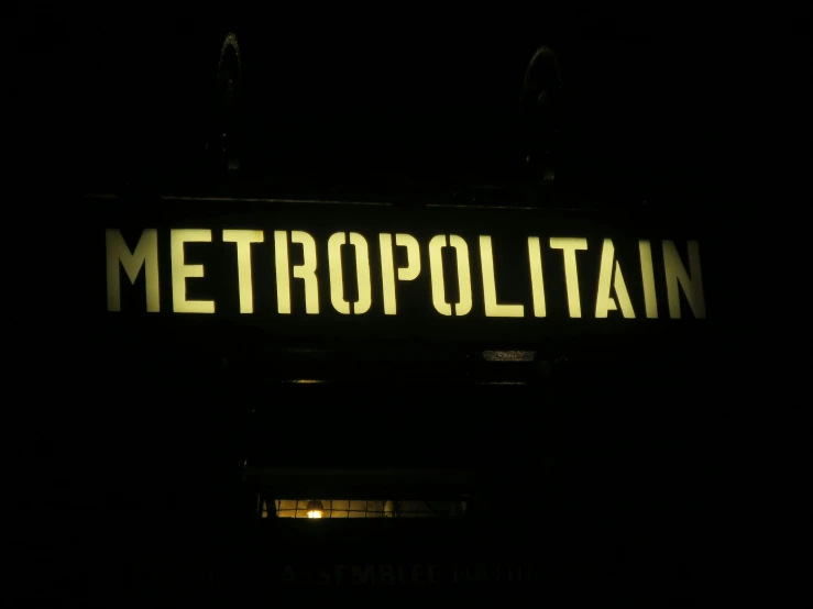 a lighted metropolatin sign sitting outside in the dark