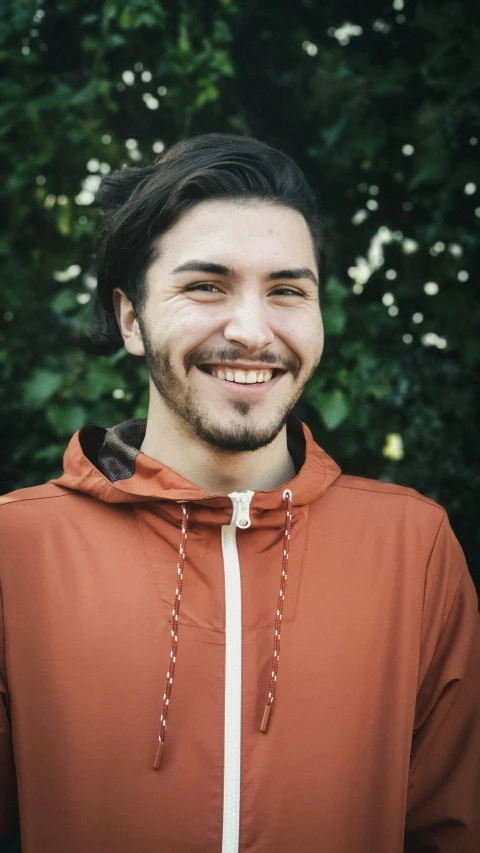 a man smiling while standing in front of green trees