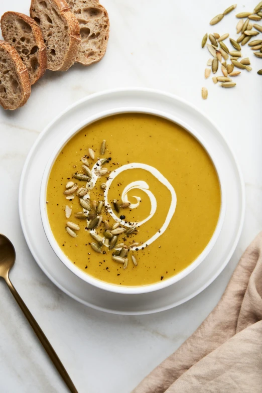 a bowl of ered carrot soup next to sliced bread