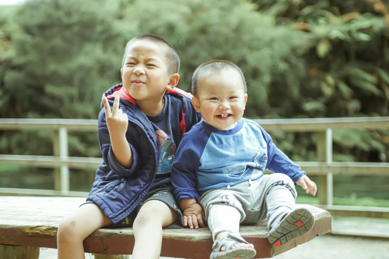 the two small boys are sitting on the park bench