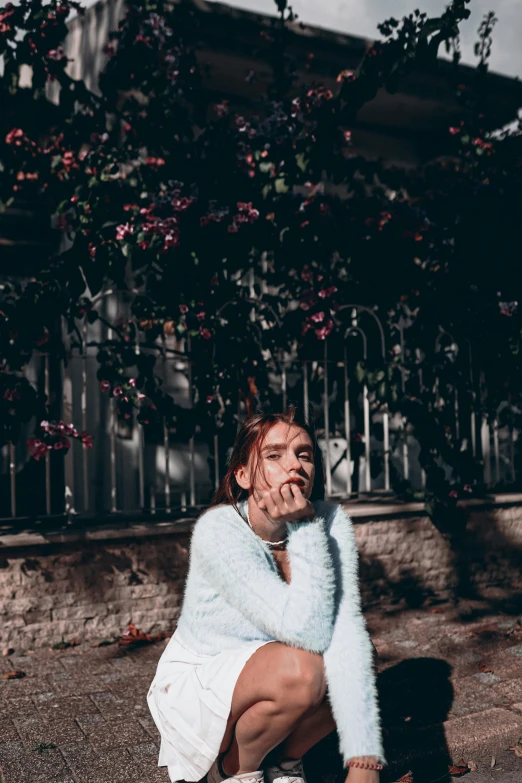 a woman wearing a white sweater sitting on the ground