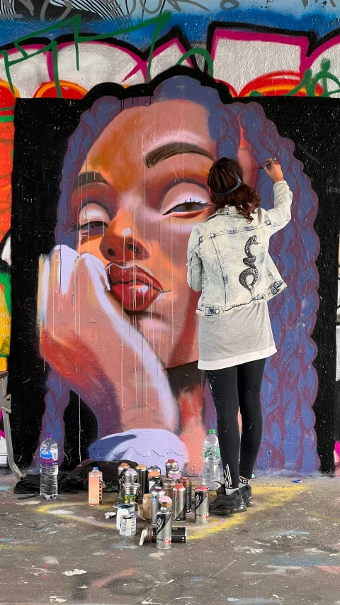 a woman standing next to a wall with art work on it