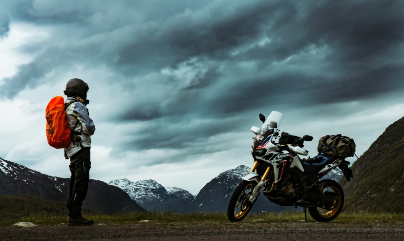 a couple of people with backpacks standing beside a motorcycle