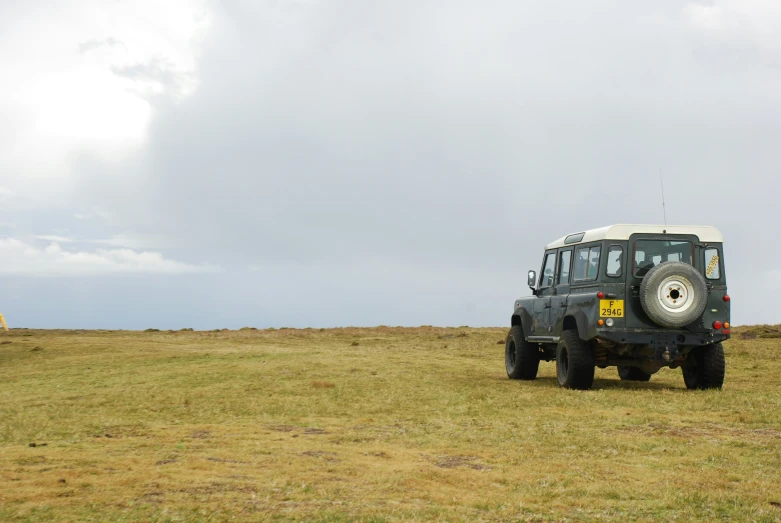 a jeep driving in a vast field with some people nearby