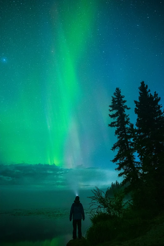 man looking up at beautiful sky with aurora over a hill