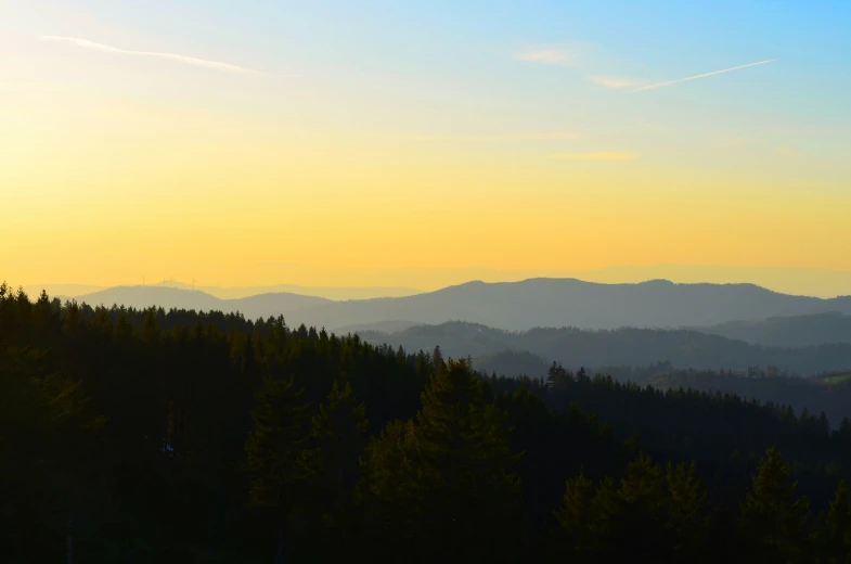 the sun setting behind mountain ranges with forest