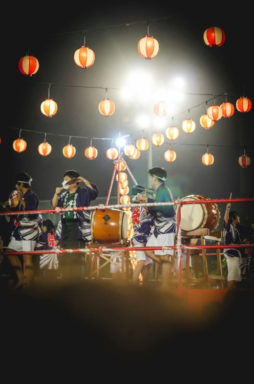 a group of drummers in a dark arena with chinese lanterns above