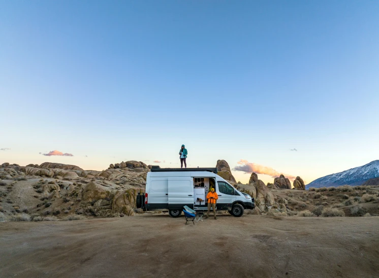 a van with a man standing on top of it sitting in front of some rock formations