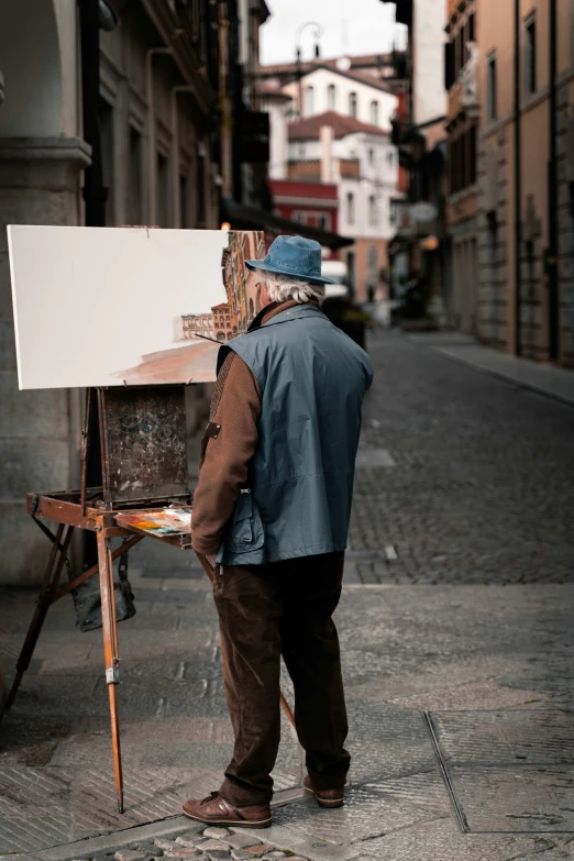 an old man standing next to a large painting easel