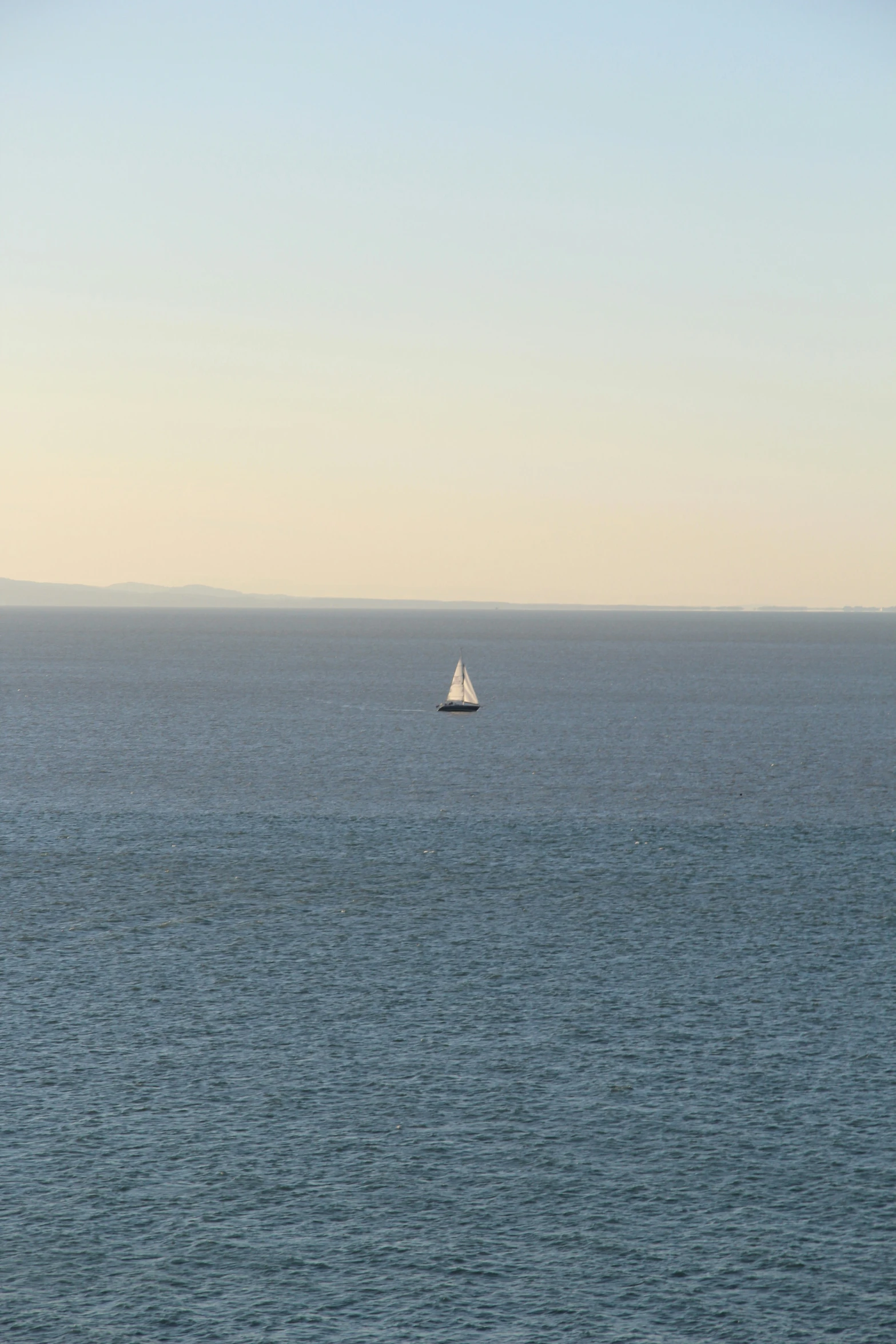 a lone white sailboat in the middle of the ocean