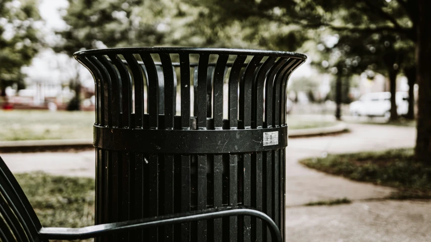 a park has a black trash can sitting outside