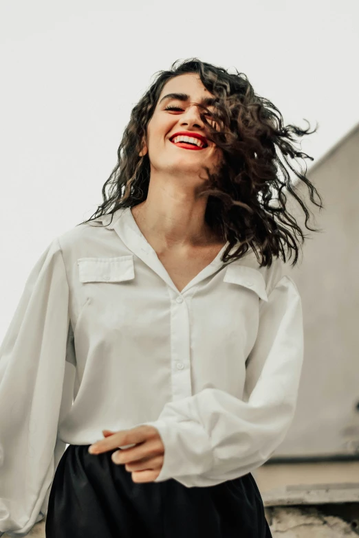 a woman in a white shirt smiles while standing next to a building